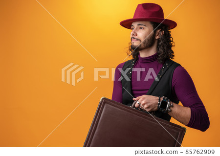 Young man with cirly long hair showing a briefcase against yellow background. 85762909