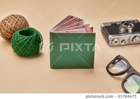 Photo book with green cover, old vintage camera, glasses and two colorful skeins of jute twine on beige studio background. Close up, copy space Photo book with green cover, old vintage camera, glasses and two colorful skeins of jute twine on beige studio background. Close up, copy space 85764475