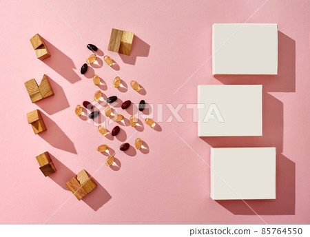 Three small cardboard boxes with no logo, scattered colorful capsules and wooden blocks of different shapes on pink background. Close up, copy space 85764550