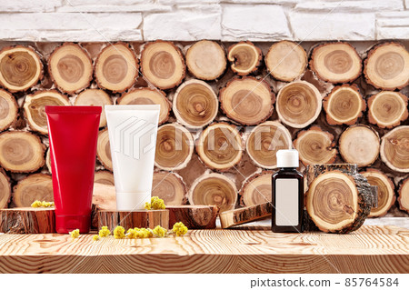 Two colorful cosmetic tubes and brown plastic bottle with branding area, small buds of blooming yellow flowers on wooden surface. Close up, copy space 85764584
