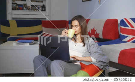 A young woman is sitting in a room at a computer, looking through a news feed. Leisure. A young woman is sitting in a room at a computer, looking through a news feed. Leisure. 85765032