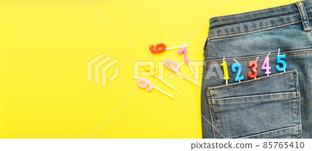 Burning birthday candles sticking out of the back pocket of blue jeans on yellow background Number 0-9 Burning birthday candles sticking out of the back pocket of blue jeans on yellow background Number 0-9 85765410