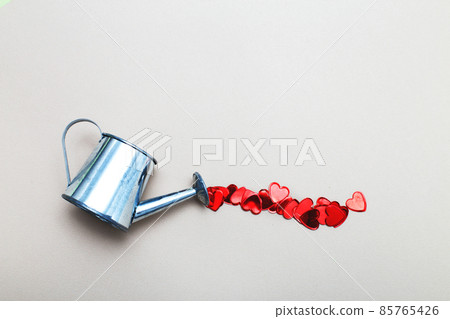 silver watering can pouring hearts on a light beige background. Valentines background, love, date concept silver watering can pouring hearts on a light beige background. Valentines background, love, date concept 85765426
