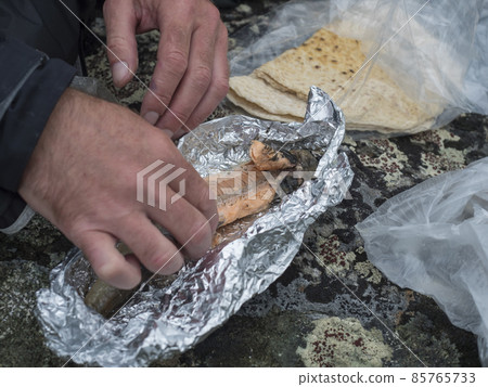 Man hands eating freshly smoked brown trout in tinfoil with traditional saami flatbread bread bought in sami village in Sweden Lapland Man hands eating freshly smoked brown trout in tinfoil with traditional saami flatbread bread bought in sami village in Sweden Lapland 85765733