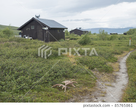 View of mountain hut STF Laddejahka fjallstuga cabin with moose antlers lying next to path. Lapland landscape Sweden at Padjelantaleden hiking trail. Summer moody sky 85765861