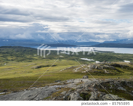 Lapland landscape at Virihaure lake with winding river, green mountains, birch trees and plain with big boulders. Sweden summer cloudy day, wild nature, Padjelantaleden hiking trail. 85765895