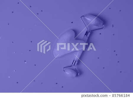 Roller and gua sha facial massage tools on a violet background with sparkles in the shape of hearts. Skin care, beauty and health concept. Color of the Year 2022 Roller and gua sha facial massage tools on a violet background with sparkles in the shape of hearts. Skin care, beauty and health concept. Color of the Year 2022 85766184