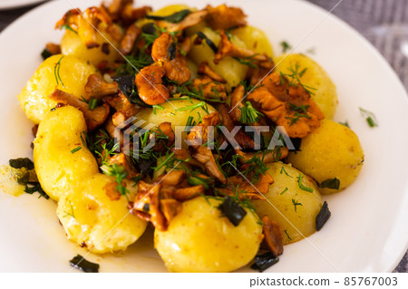 baked potatoes with chanterelles, served with herbs on white plate 85767003