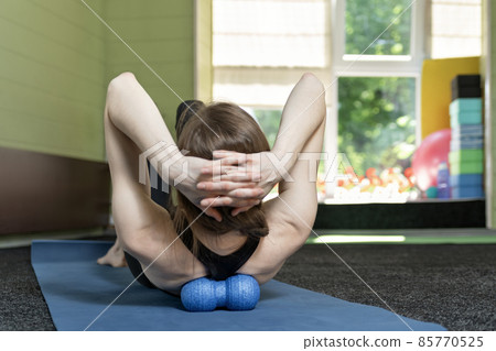 Girl lies on yoga mat and does back massage with roller for physiotherapy. Myofascial release with foam ball. Back view 85770525