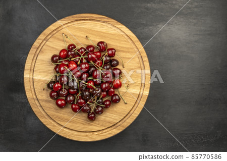 Fresh ripe sour cherries on wooden plate on gray background. Red juicy cherries. Sweet cherry background. 85770586