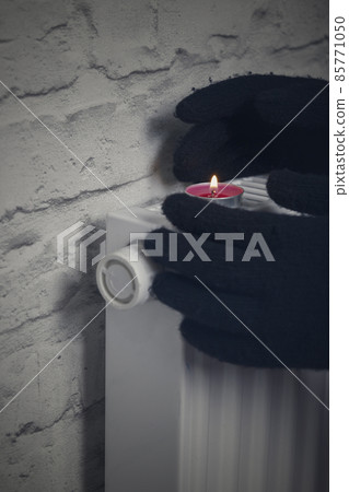 A woman's hand in winter gloves warms her hands from a heating battery. The concept of the cost of heating services, the increase in prices for utilities. Lack of heat. A woman's hand in winter gloves warms her hands from a heating battery. The concept of the cost of heating services, the increase in prices for utilities. Lack of heat. 85771050