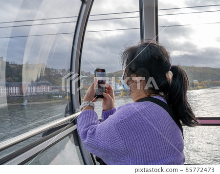 A middle-aged Asian woman with a smartphone wearing face mask in a cable car 85772473