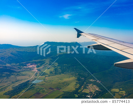 View of airplane wing, blue skies and green land during landing. Airplane window view. 85774413