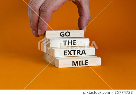Go the extra mile symbol. Wooden blocks with words 'Go the extra mile'. Businessman hand. Beautiful orange background. Business and go the extra mile concept. Copy space. 85774728