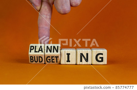 Budgeting and planning symbol. Businessman turns wooden cubes and changes the word planning to budgeting. Beautiful orange background, copy space. Business, budgeting and planning concept. 85774777