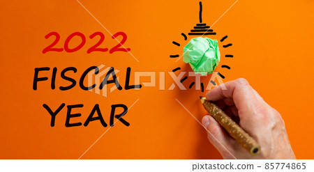 2022 fiscal new year symbol. Businessman writing words '2022 fiscal year', isolated on beautiful orange background. Light bulb icon. Business and 2022 fiscal new year concept. Copy space. 2022 fiscal new year symbol. Businessman writing words '2022 fiscal year', isolated on beautiful orange background. Light bulb icon. Business and 2022 fiscal new year concept. Copy space. 85774865