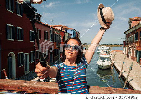 Influence media Burano Italy. Paint building house in Europe Venezia city. Travel photographer blogger girl with smartphone in Venice island color street. Freedom, summer travel, profession concept. 85774962