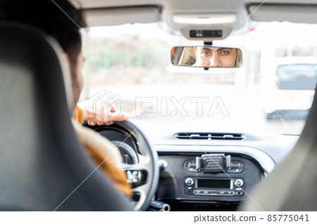 Man holding driving wheel riding car looking in rearview mirror at daytime Man holding driving wheel riding car looking in rearview mirror at daytime 85775041