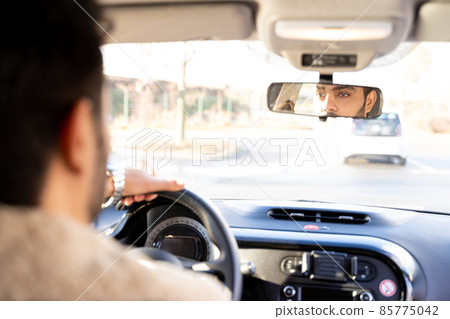 Man holding driving wheel riding car looking in rearview mirror at daytime Man holding driving wheel riding car looking in rearview mirror at daytime 85775042