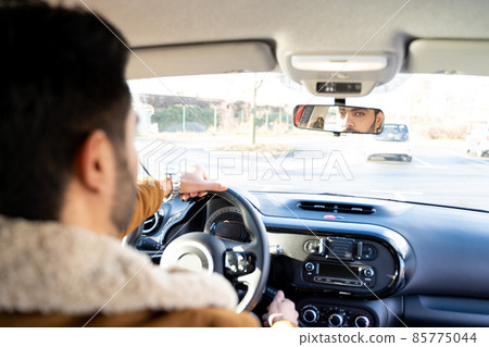 Man holding driving wheel riding car looking in rearview mirror at daytime Man holding driving wheel riding car looking in rearview mirror at daytime 85775044