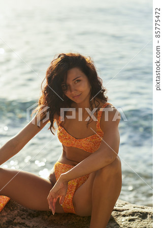 Beach Girl Model in Orange Bikini on the Rocky Deserted Seashore During Summer Beach Holidays 85775472