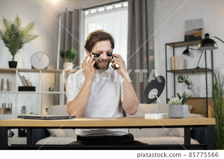 Handsome bearded man talks on the phone while taking cosmetic procedures with patches Handsome bearded man talks on the phone while taking cosmetic procedures with patches 85775566