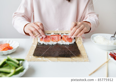 Sushi preparation process, the girl makes sushi with different flavors - fresh salmon, caviar, avocado, cucumber, ginger, rice. 85775912