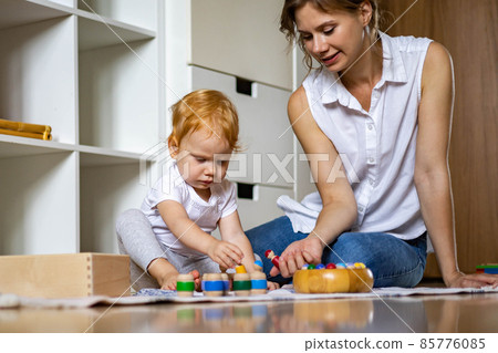 Smiling mother and baby playing wooden toy educational game gnomes in barrels spending time together 85776085