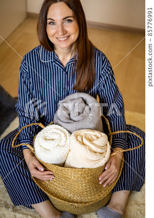 Portrait of happy young domestic woman in pajamas posing with straw basket for linens storage 85776991