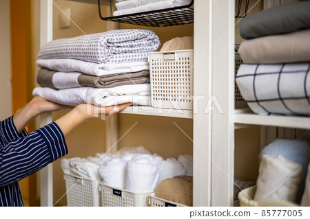 Domestic woman in pajamas neatly putting folded linens into cupboard vertical storage Marie Kondo 85777005