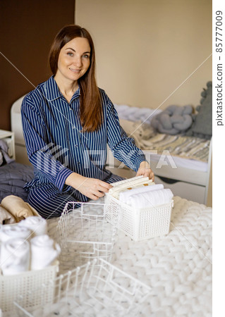Modern housewife putting neatly folded towels, pillowcases, duvet covers into plastic metallic case Modern housewife putting neatly folded towels, pillowcases, duvet covers into plastic metallic case 85777009