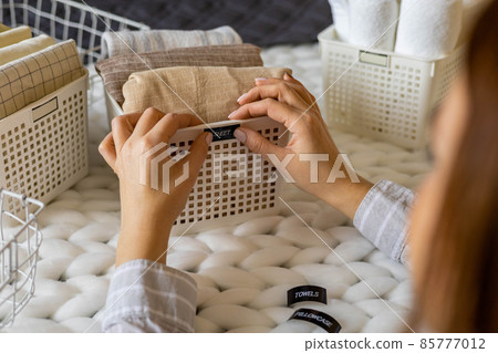 Woman hands neatly folded linens and towels use Marie Kondo method with sticky label tags Woman hands neatly folded linens and towels use Marie Kondo method with sticky label tags 85777012