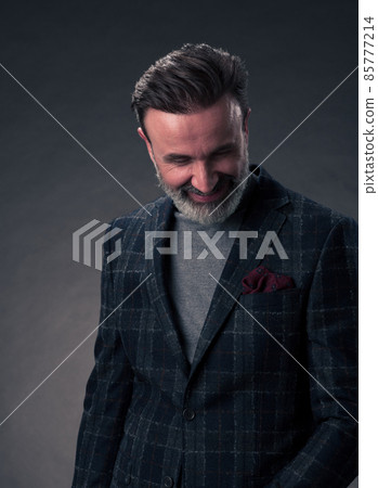 Portrait of a stylish elegant senior businessman with a beard and casual business clothes in photo studio isolated on dark background gesturing with hands 85777214