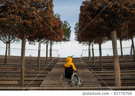 Woman in a wheelchair in front of the stairs in the street in winter. 85779708