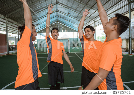 Futsal players gather in a circle raising their hands 85785761