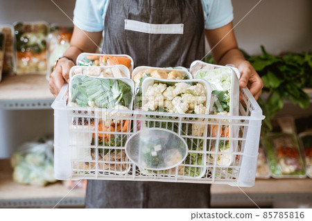 A seller wearing an apron carrying a basket of vegetables A seller wearing an apron carrying a basket of vegetables 85785816