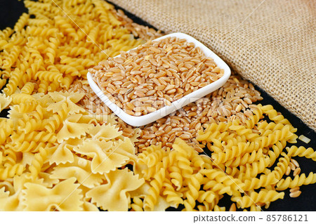 some dry wheat and different shapes of pasta standing on black background,close-up of macaroni and wheat together, some dry wheat and different shapes of pasta standing on black background,close-up of macaroni and wheat together, 85786121