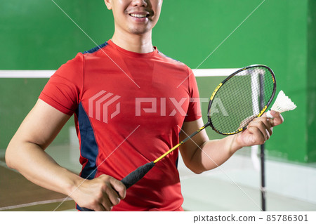 player's hand holding racket and shuttle on indoor court 85786301