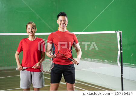 Two confident badminton players holding rackets standing against net background 85786434