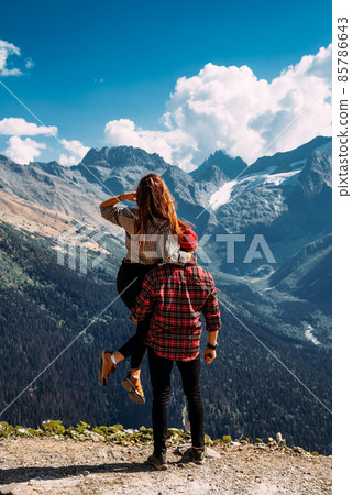 A traveling couple in plaid shirts against the backdrop of mountains. Two tourists on the top of the mountain. A man and a woman in the mountains. Two travelers enjoy climbing the mountain. Copy space 85786643