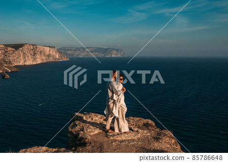 A man embraces a beautiful woman on the edge of a cliff by the sea. A couple in love at sunset. Beautiful couple meets sunset by the sea. Happy couple having fun on the coast. Copy space 85786648