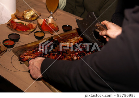 Waiter chops juicy barbecue ribs when serving to restaurant customers 85786985
