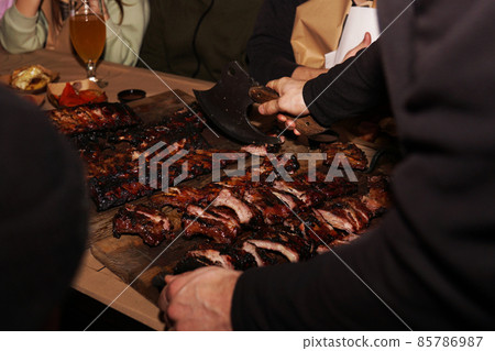 Waiter chops juicy barbecue ribs when serving to restaurant customers 85786987