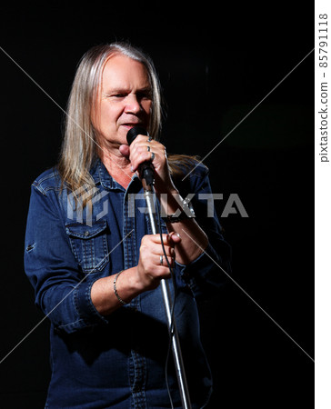 elderly man with long gray hair sings into a microphone 85791118