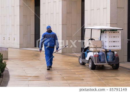 Man dressed in a work uniform with a net to remove leaves from the pool. Electric vehicle or golf car Man dressed in a work uniform with a net to remove leaves from the pool. Electric vehicle or golf car 85791149