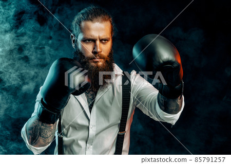 Serious bearded man in white shirt wears boxing gloves and ready to fight in smoke. Man self defense Serious bearded man in white shirt wears boxing gloves and ready to fight in smoke. Man self defense 85791257