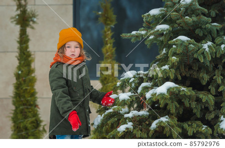 Winter Christmas tree outdoors. Kid take care about snow-covered fir tree. Christmas tree farm on a sunny winter day. Green energy of the future. Sustainable. Child in winter warm clothes Winter Christmas tree outdoors. Kid take care about snow-covered fir tree. Christmas tree farm on a sunny winter day. Green energy of the future. Sustainable. Child in winter warm clothes 85792976