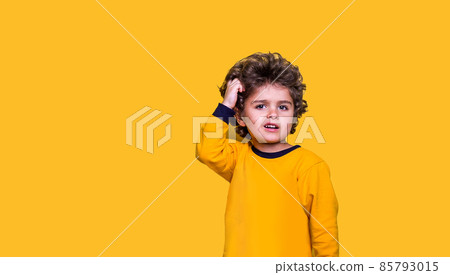 Smart funny curly kid scratches his head while thinking. Little wunderkind ready to go to school isolated on yellow background. Child looking up while thinking Smart funny curly kid scratches his head while thinking. Little wunderkind ready to go to school isolated on yellow background. Child looking up while thinking 85793015