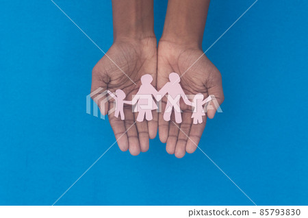 Hand holding family figure cutout top view. World health day Protection against domestic violence, healthcare and medical background. Foster care, homeless support and social distancing concept. Hand holding family figure cutout top view. World health day Protection against domestic violence, healthcare and medical background. Foster care, homeless support and social distancing concept. 85793830