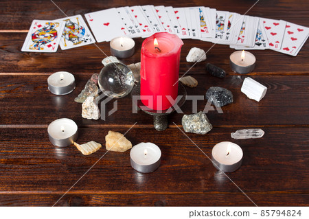 On the table are fortune-telling cards, a magic ball, magic crystals and a lighted candle.Magic sessions with clairvoyance cards. Card reading by candlelight On the table are fortune-telling cards, a magic ball, magic crystals and a lighted candle.Magic sessions with clairvoyance cards. Card reading by candlelight 85794824